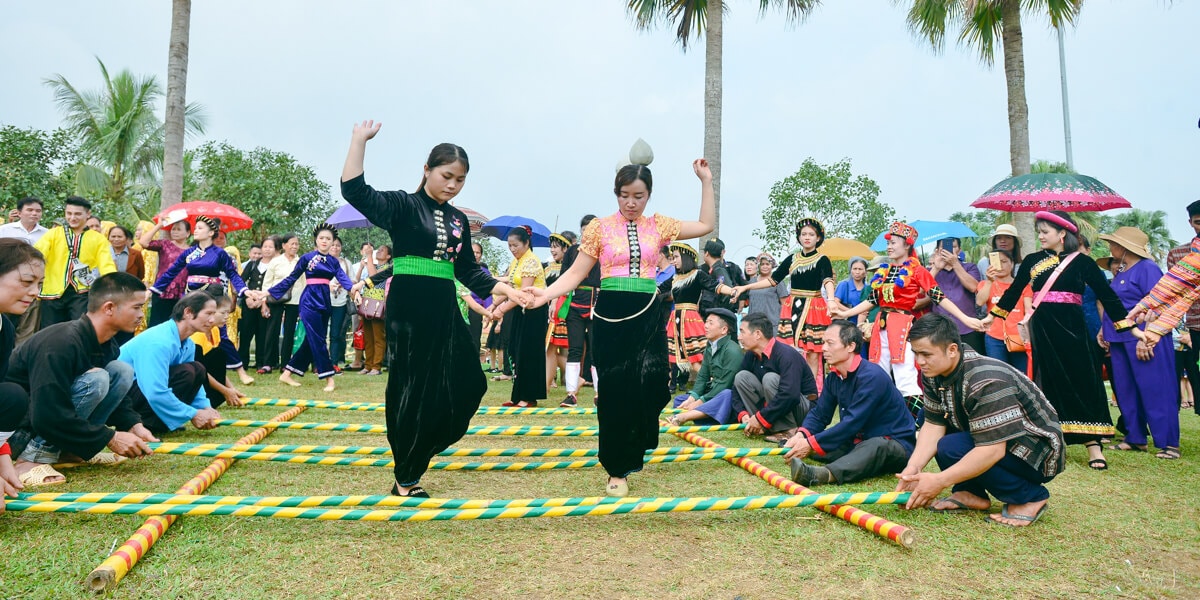 Dancers hop and weave between clapping bamboo poles that are rhythmically tapped by others on the ground